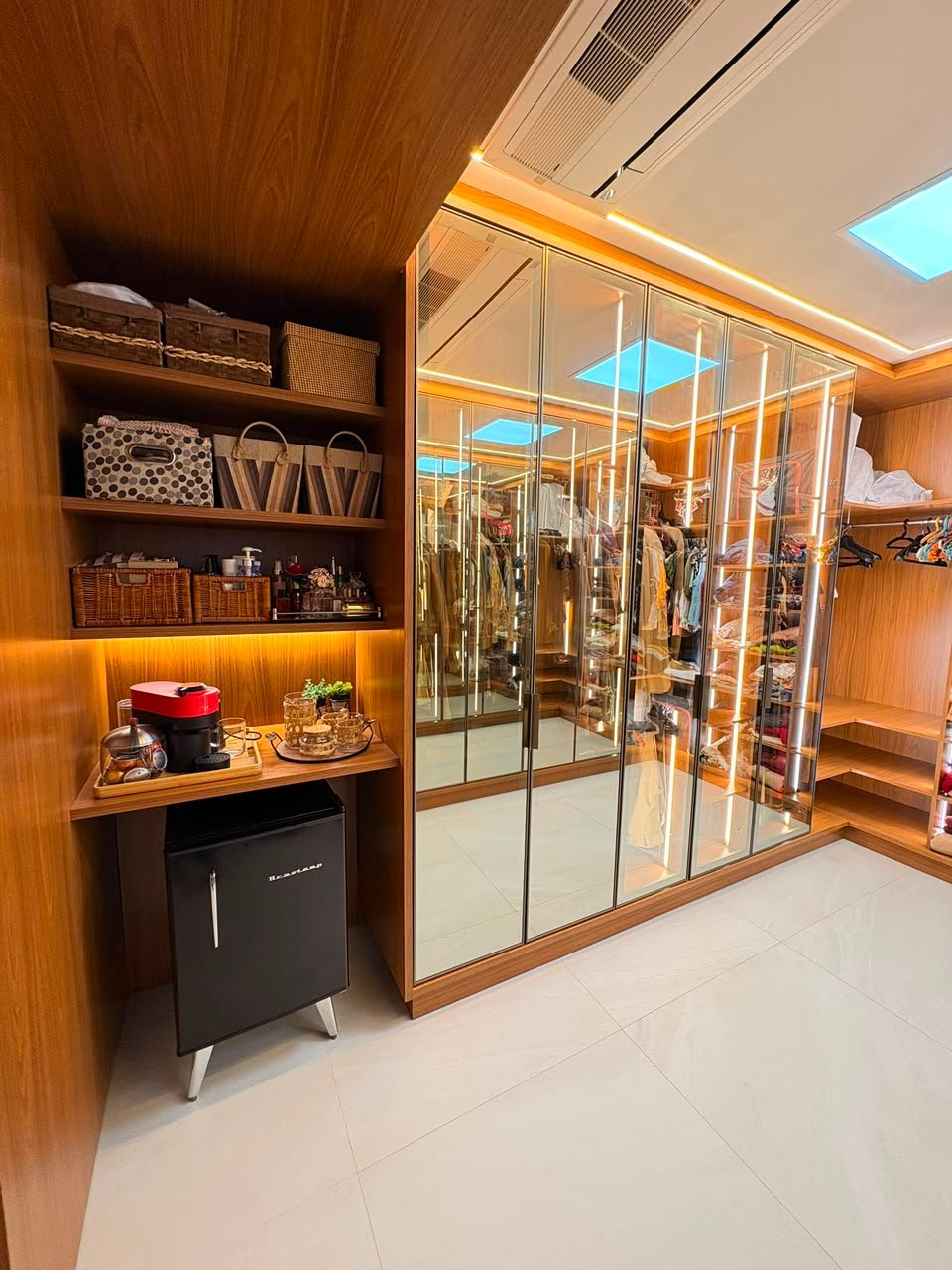 Closet planejado pela Bayerl Marcenaria com portas espelhadas, iluminação em LED e frigobar integrado